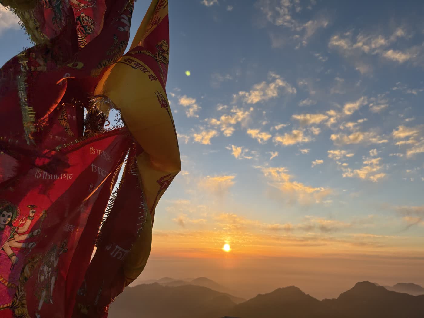A red Devi prayer flag billowing against a sunset sky over the Himalayas